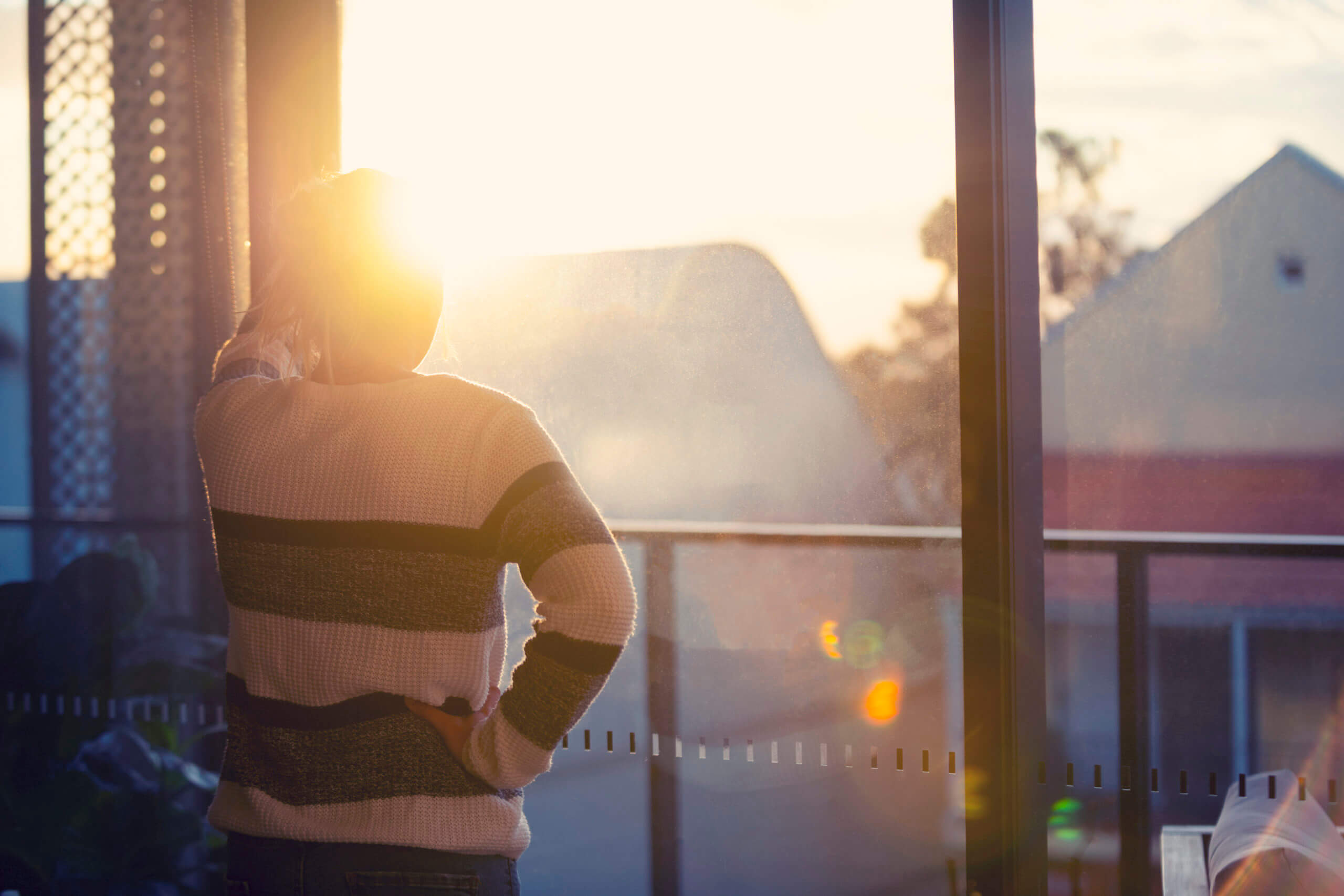 Woman looking through the window at sunset. She is alone and looks a little ad or depressed.